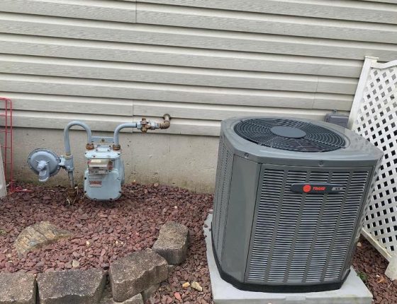 air conditioning unit sitting on maroon gravel next to white lattice fence