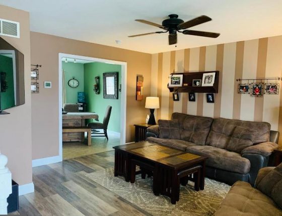 living room furniture sitting beneath ceiling fan next to kitchen in new home for sale